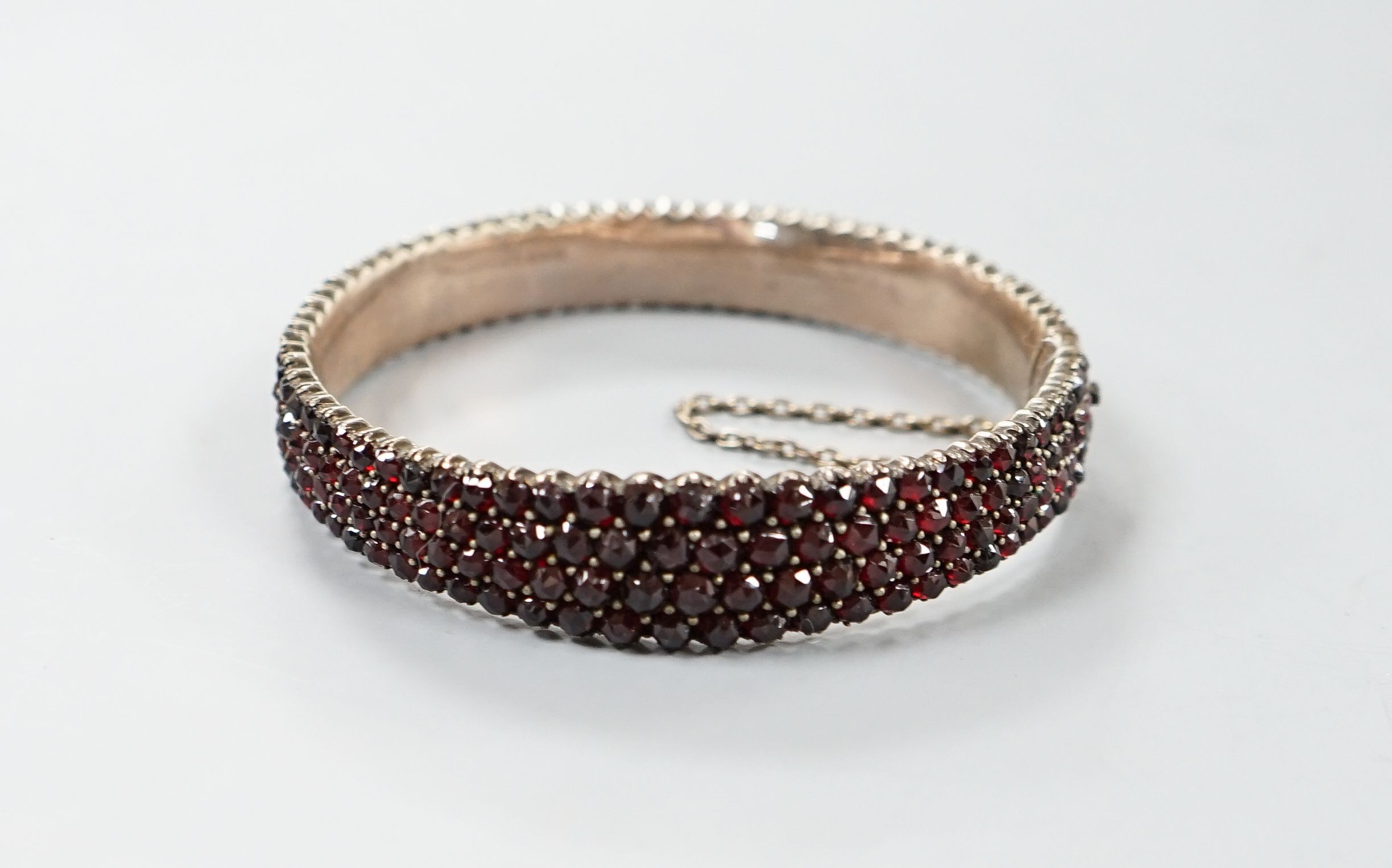 A late Victorian gilt white metal and garnet encrusted hinged bangle (stone missing).